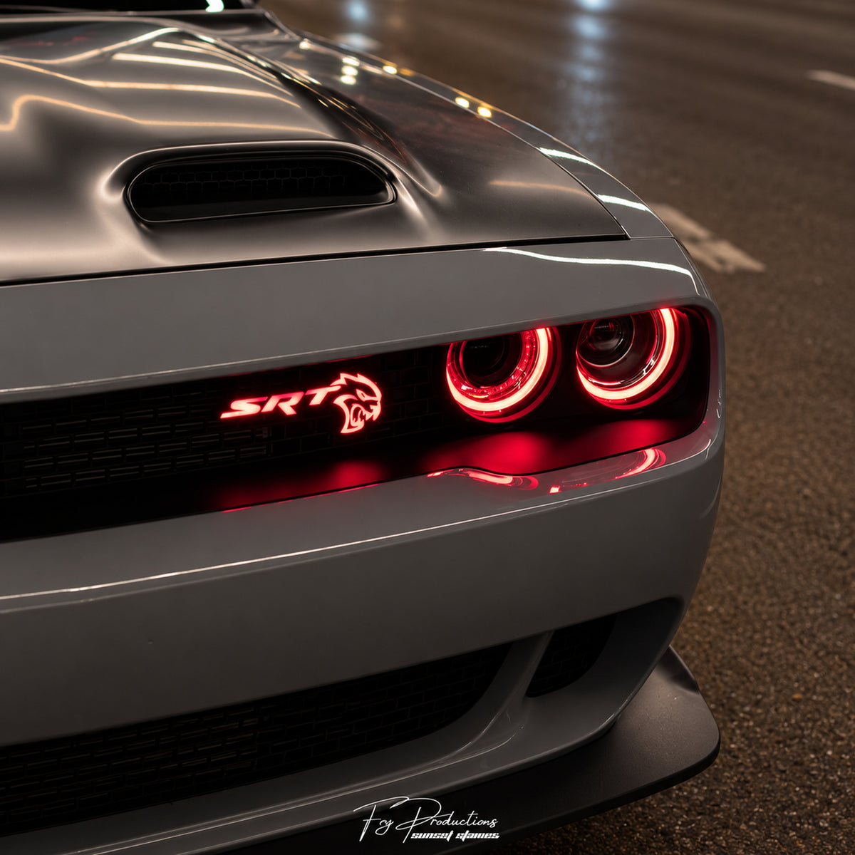 Red illuminated SRT Hellcat grille emblem on a gray Dodge Challenger at night